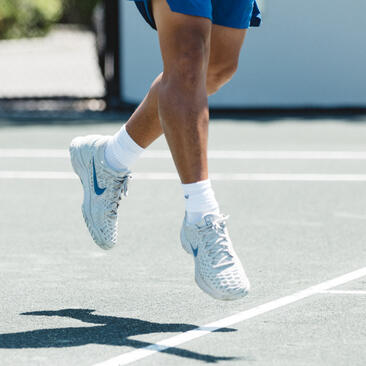 Player's feet mid-stride on Amanyara's tennis court in white trainers and socks.