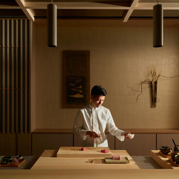 Chef en el comedor Nama del hotel Aman New York, preparando un plato con precisión.