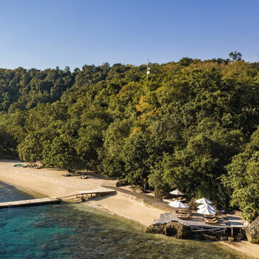 Amanwana's sandy beach cove bordered by dense tropical forest and turquoise waters.