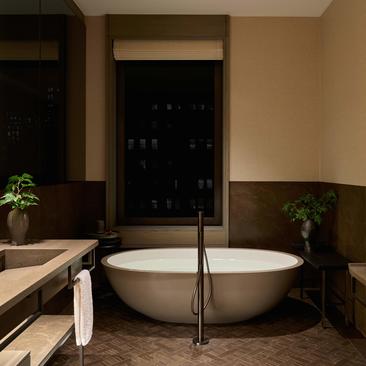 Banheiro da Aman Suite com banheira redonda branca, espelho iluminado e plantas decorativas, no hotel Aman New York.