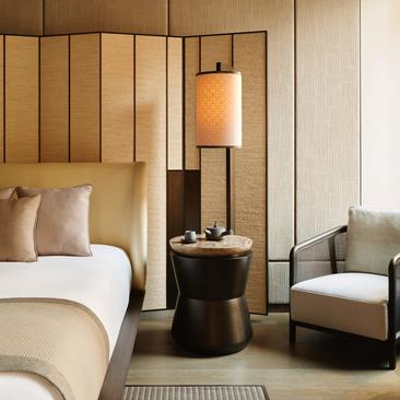 Suite con letto principale, poltrona e lampada in legno naturale all'Aman New York.