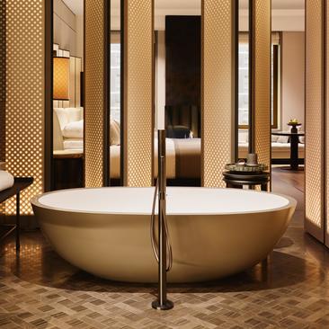 Oval freestanding bathtub in a wood-paneled bathroom at Aman New York, with floor-mounted faucet and mirrored backdrop.