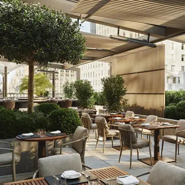 Terraço de jardim do Aman New York com mesas de jantar ao ar livre, plantas e arquitetura moderna.