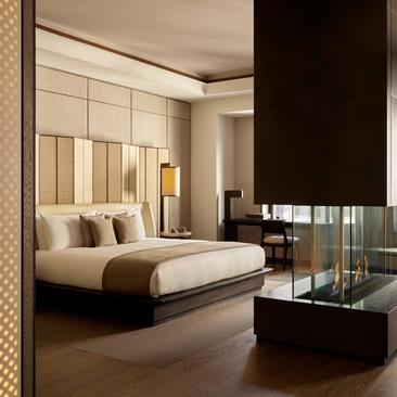 Quarto Grand Suite com cama estofada, painel de madeira clara e lareira moderna no Aman New York.