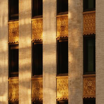 Architectural facade of Aman New York with alternating lit and dark window bays at sunset.