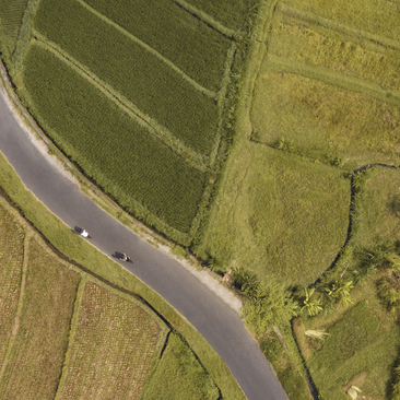 Aerial view of a cyclist riding along a curved road beside a river at Amankila.