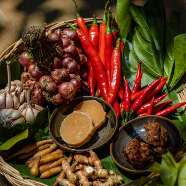 Cooking class ingredients at Amansara: red chillies, garlic, shallots, and paste in bowls arranged on green leaves.
