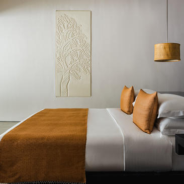 Principal bedroom at Amansara with ochre bedding, decorative cushions, and botanical wall art.