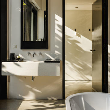 Amansara bathroom with floating white sink, black-framed mirror, and glass-enclosed shower filled with natural light.