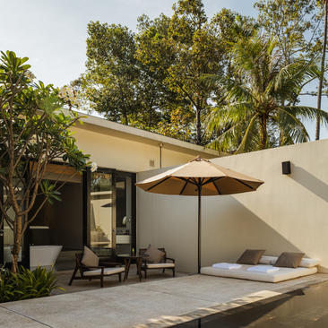 Amansara pavilion with cream-coloured walls, shaded seating area and tropical gardens in Cambodia.