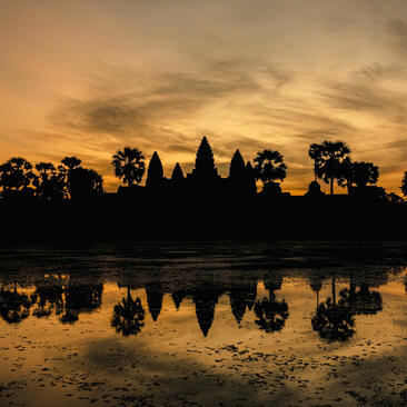 Silhouette of Angkor Wat's towers reflected in still water at sunrise, Amansara, Cambodia.
