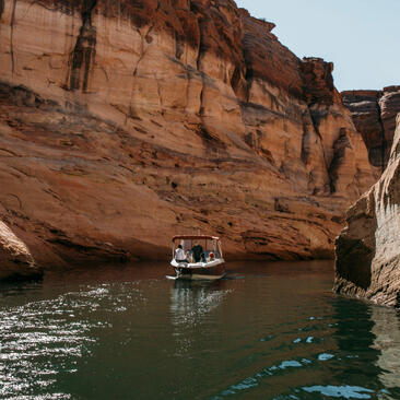 Family exploring Lake Powell by boat at Amangiri, with red rock cliffs rising above.
