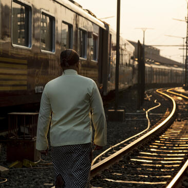 A guest stands on railway tracks beside a train at Amanjiwo, Indonesia, at golden hour.