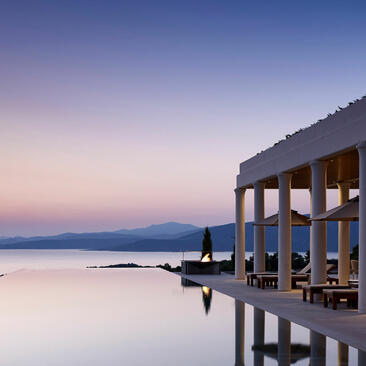 Villa 20 at Amanzoe resort overlooking calm waters at dusk, with illuminated columns framing the serene coastal view.