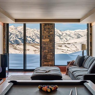 Modern living room at Amangani with floor-to-ceiling windows framing snow-capped mountains and alpine lake views.