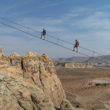 Two people zip-lining across a desert landscape at Amangiri, Utah.