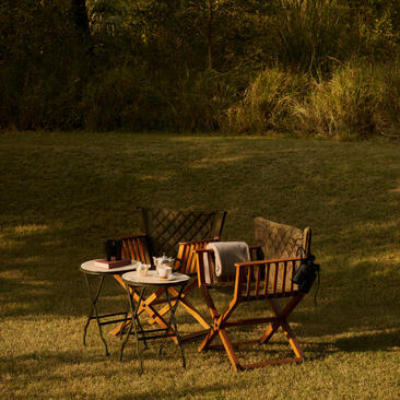Bird watching setup at Aman-i-Khas with chairs and binoculars overlooking grassland at dusk.