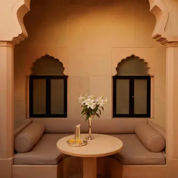 Courtyard Haveli Suite with arched alcove seating, two dark-framed windows, and round table with flowers at Amanbagh.