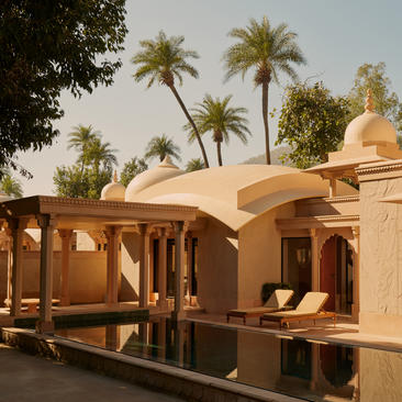 Pool pavilion at Amanbagh with terracotta dome and wooden columns, framed by palm trees.