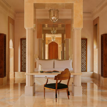 Terrace Haveli Suite bedroom at Amanbagh with symmetrical archways, polished stone floor, and a single wooden chair in the centre.