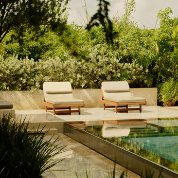 Deux chaises longues crèmes face à une piscine à débordement, entourées de végétation luxuriante à Amanera, resort en République Dominicaine.