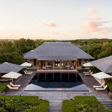 Amanyara villa with central pavilion, infinity pool and manicured grounds overlooking tropical landscape at dusk.