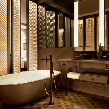 Deluxe suite bathroom at Aman New York with freestanding soaking tub, wooden vanity, and warm lighting.