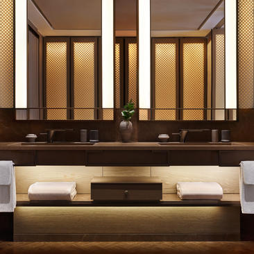 Bagno della Deluxe Suite con doppio lavabo in legno scuro e specchi illuminati, Aman New York.