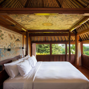 Principal bedroom in a duplex pool suite at Amandari, featuring a wooden bed with white linens and traditional Balinese architectural details.
