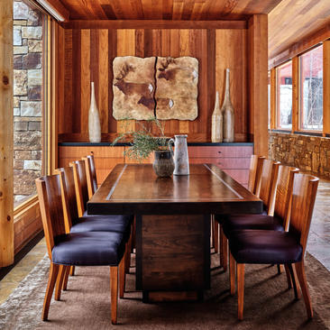 Dining area at Amangani with wooden table, chairs upholstered in deep purple fabric, and warm wood panelling throughout the room.