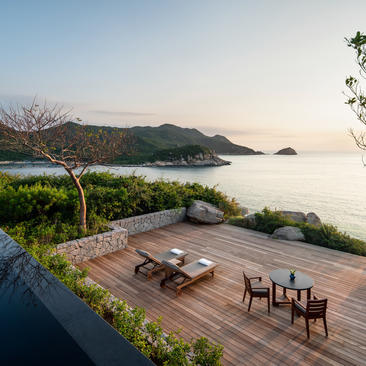 Ocean pool villa terrace at Amanoi with wooden deck, dining chairs, and views across calm waters to distant mountains.