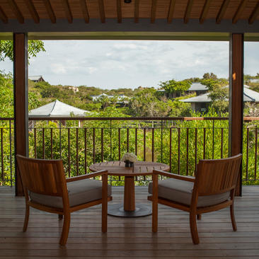 Two wooden chairs positioned on a wooden terrace at Amanoi, Vietnam, overlooking forested hills and a distant lake pavilion.