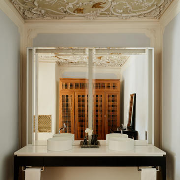 Espejo de baño con marco blanco en la suite Alcova Tiepolo de Aman Venice, reflejando detalles arquitectónicos del hotel.