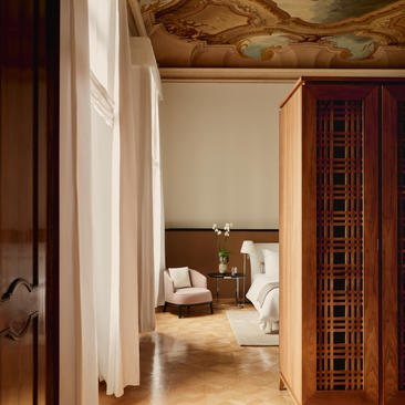 Hallway leading to principal bedroom in Coccinas apartment at Aman Venice hotel, with wooden doors and terracotta flooring.