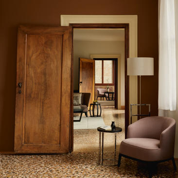Suite connectedora au Grand Canal à Aman Venice, avec portes en bois et fauteuil rose pâle.