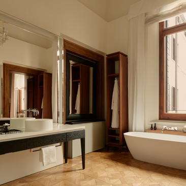 Bathroom at Aman Venice with freestanding bathtub, dual vanity and canal views through wooden-framed windows.