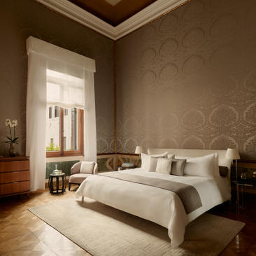 Serene bedroom at Aman Venice with canal views, featuring a bed dressed in neutral linens and warm taupe walls.
