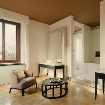 Bathroom with walk-in shower and sitting area at Aman Venice hotel, featuring warm terracotta ceiling and cream walls.