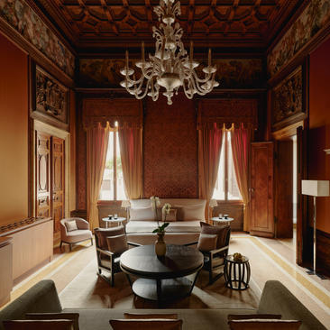 Sansovino Stanza bedroom at Aman Venice, featuring terracotta walls, chandelier, and classical furnishings.