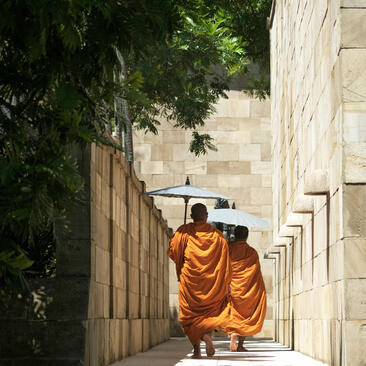 Monks in saffron robes walking through a stone corridor at Amanjiwo resort, Indonesia, during Vesak celebrations.