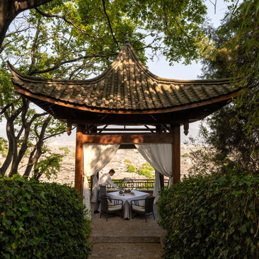 Wooden pavilion with curved roof at Amandayan, framing stone pathway and gardens beyond.