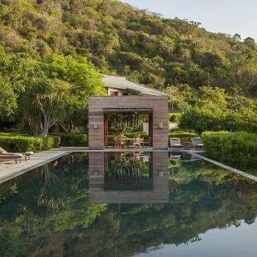 Five-bedroom bay villa with stone structure reflected in still plunge pool, surrounded by verdant hillside at Amanoi.