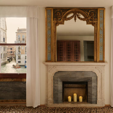 Dormitorio Suite Grand Canal con chimenea decorativa y espejo dorado en Aman Venice.
