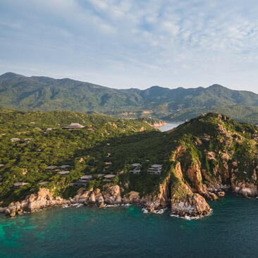 Amanoi aerial view showing clifftop resort nestled among forested hills overlooking turquoise waters of Ninh Van Bay, Vietnam.