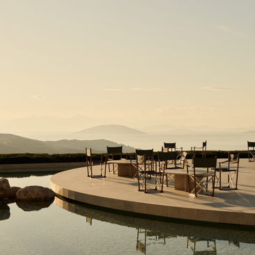 Exterior bar at Amanzoe with wooden deck overlooking still waters at dusk, Greece.