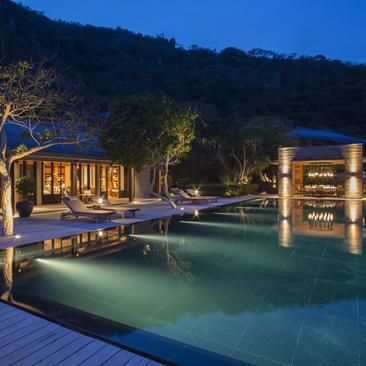 Night-time view of Amanoi's illuminated pool pavilion and dining area reflected in still water.
