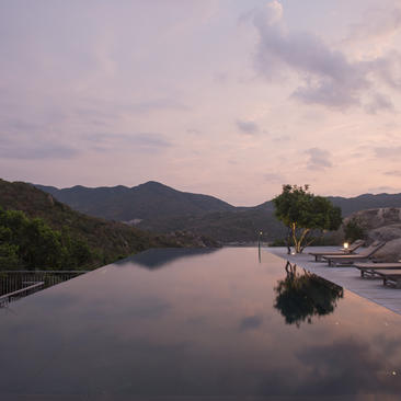 Amanoi overlooks a serene river at dusk, with mountains reflected in still waters.