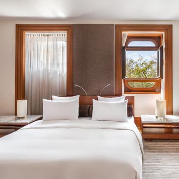 Principal bedroom at Aman Sveti Stefan with double bed, wooden doors and views to the Adriatic coast.