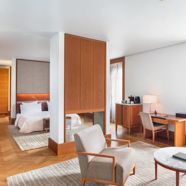 Spacious principal bedroom at Aman Sveti Stefan with wooden furnishings, separate seating area, and sea views.