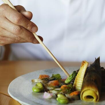 Mano con pincel decorando plato de verduras en Amanemu resort.